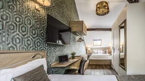 A modern hotel room with a geometric-patterned wall, a wooden desk with a laptop, a bed with white linens, and a hanging light fixture. - Chabrol Opéra (Paris)