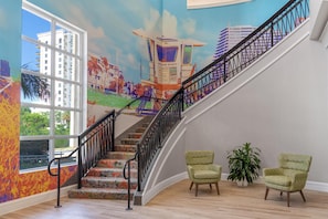 Un escalier orné d’une fresque murale, deux fauteuils verts et une plante en pot.