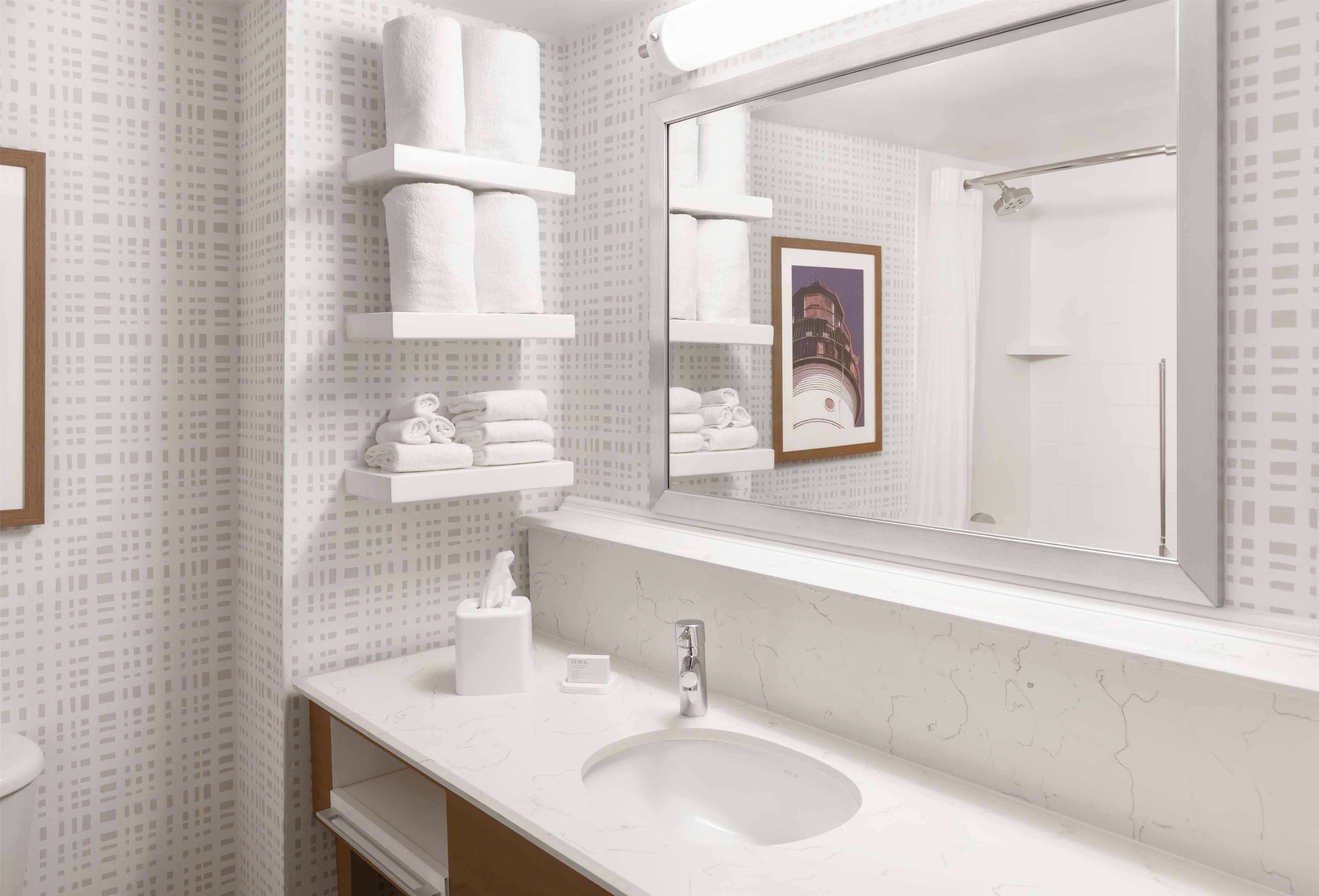 A bathroom with a white marble sink, a mirror, and shelves holding white towels.