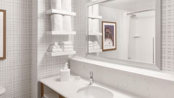 A bathroom with a white marble sink, a mirror, and shelves holding white towels.