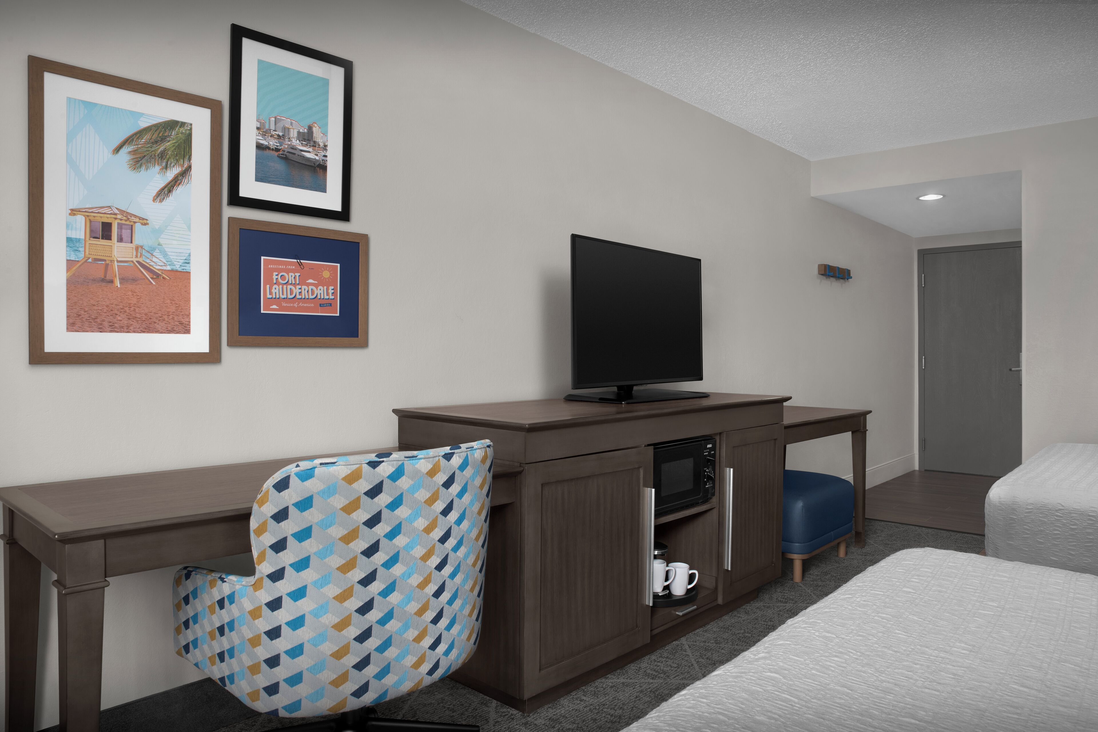 Ein Hotelzimmer mit einem Bett, einem Schreibtisch mit Fernseher, einer Kaffeemaschine und einem Sessel. An der Wand hängen gerahmte Bilder.
