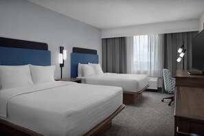 Een hotelkamer met twee bedden, een bureau, een stoel en een groot raam met gordijnen.