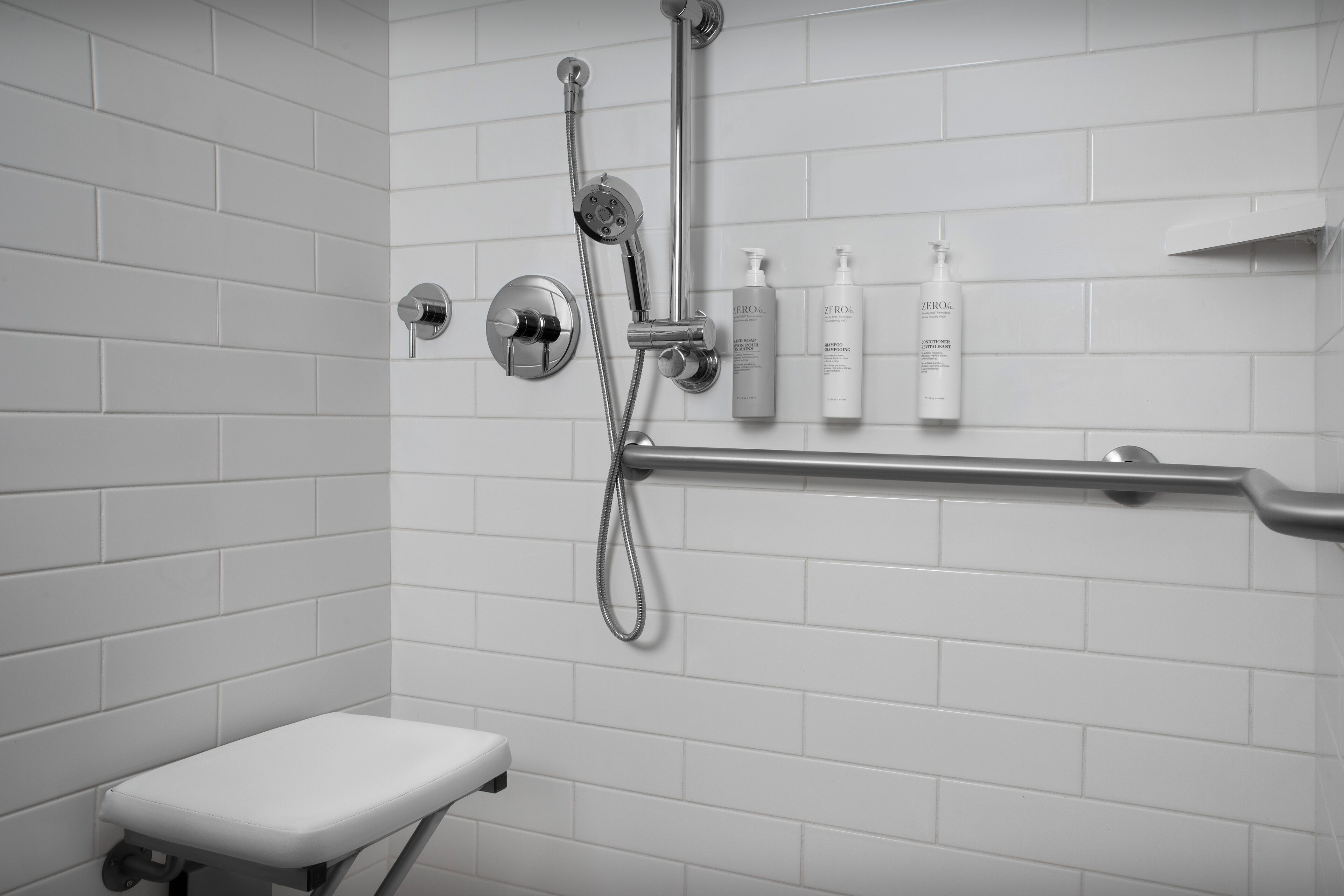 A modern bathroom with white tiles, a shower with a handheld showerhead, and a toilet.
