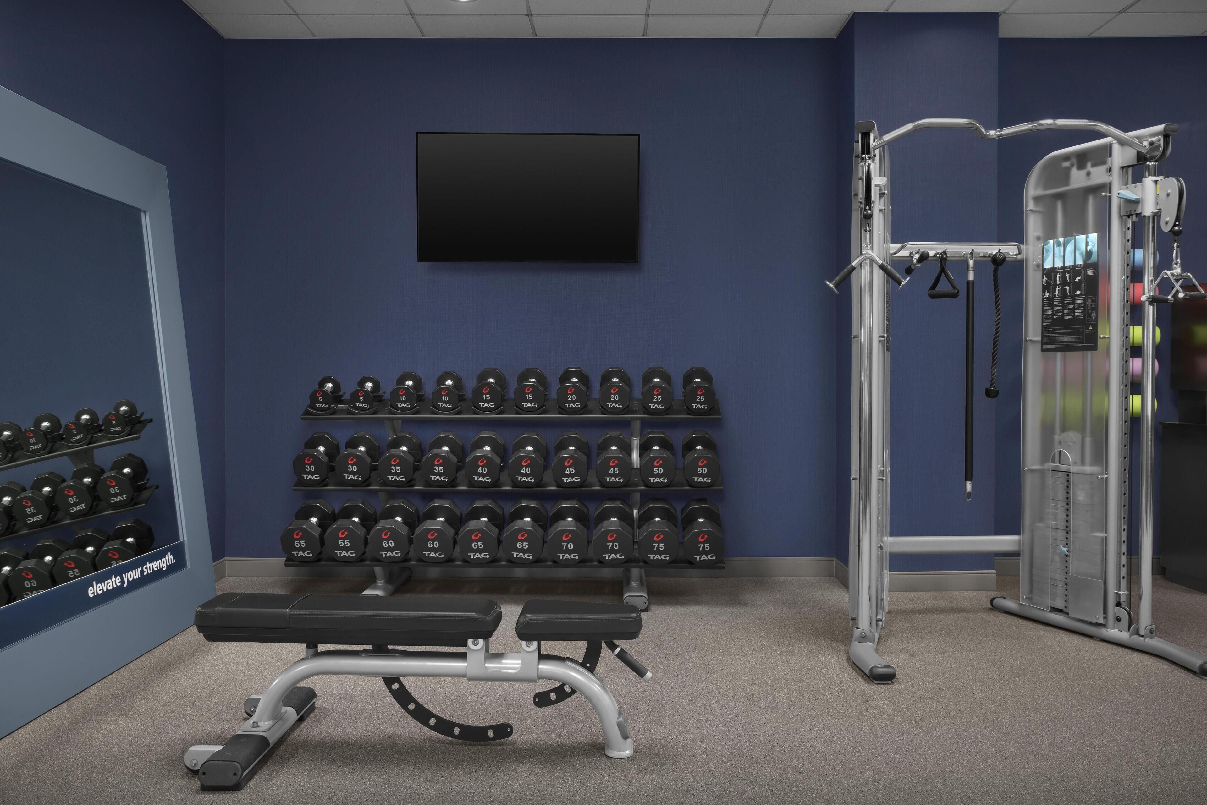 Un gimnasio con una banca, mancuernas y una máquina de pesas.