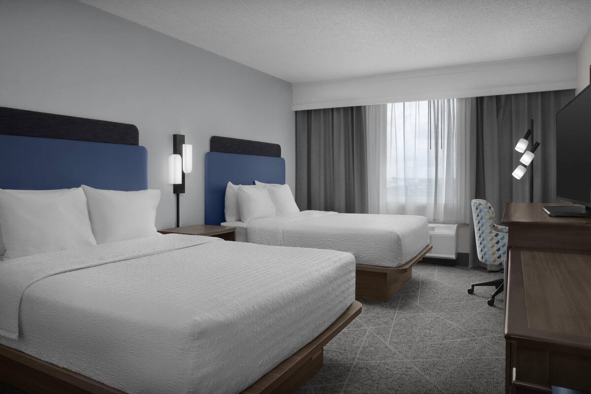 A hotel room with two beds, a desk, a chair, and a large window with curtains.