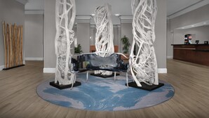 Un vestíbulo con un banco negro central, esculturas abstractas blancas, un mostrador de recepción y suelo de madera.