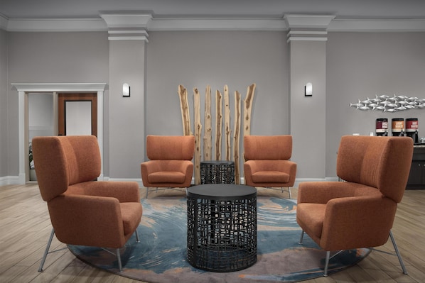 Un hall d’entrée moderne avec deux fauteuils orange, une table ronde noire et une structure décorative en bois.