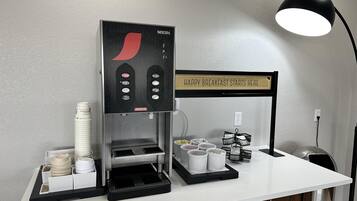 Uma máquina de café com um letreiro que diz 'HAPPY BREAKFAST STARTS HERE' e uma luminária em uma mesa.