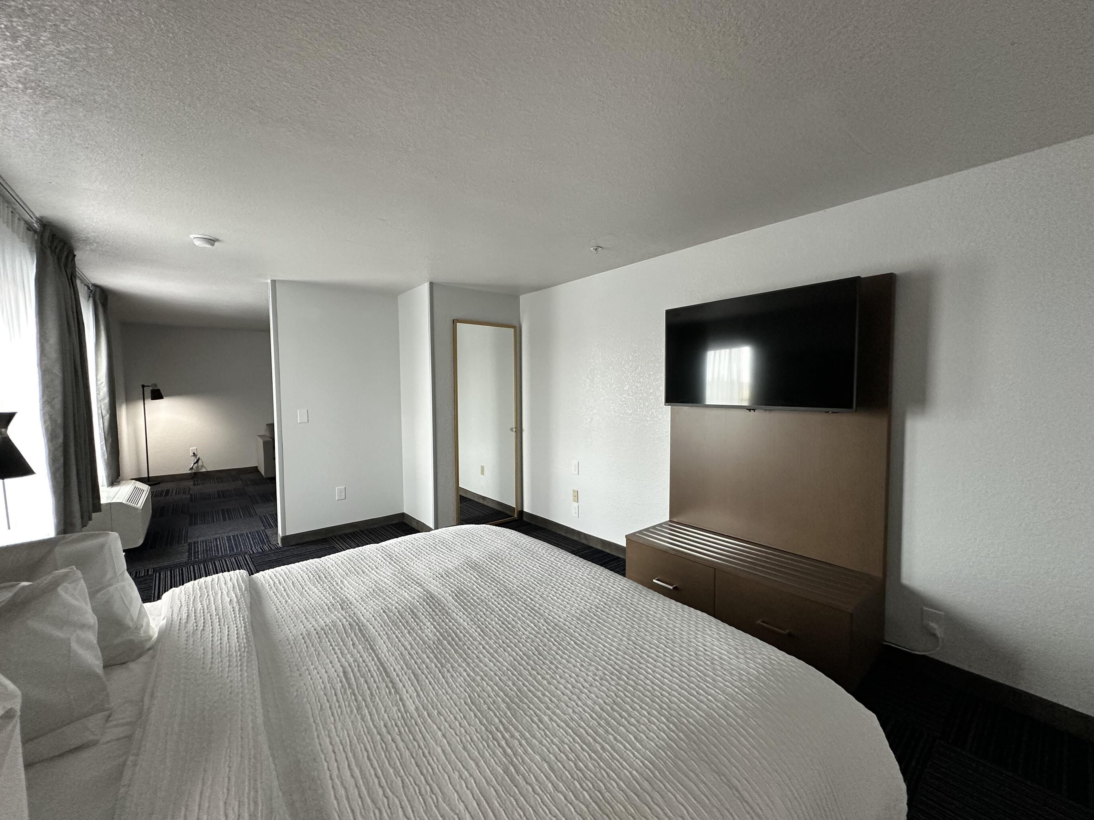 Une chambre d’hôtel avec un grand lit, un téléviseur à écran plat fixé au mur, un bureau et un miroir.
