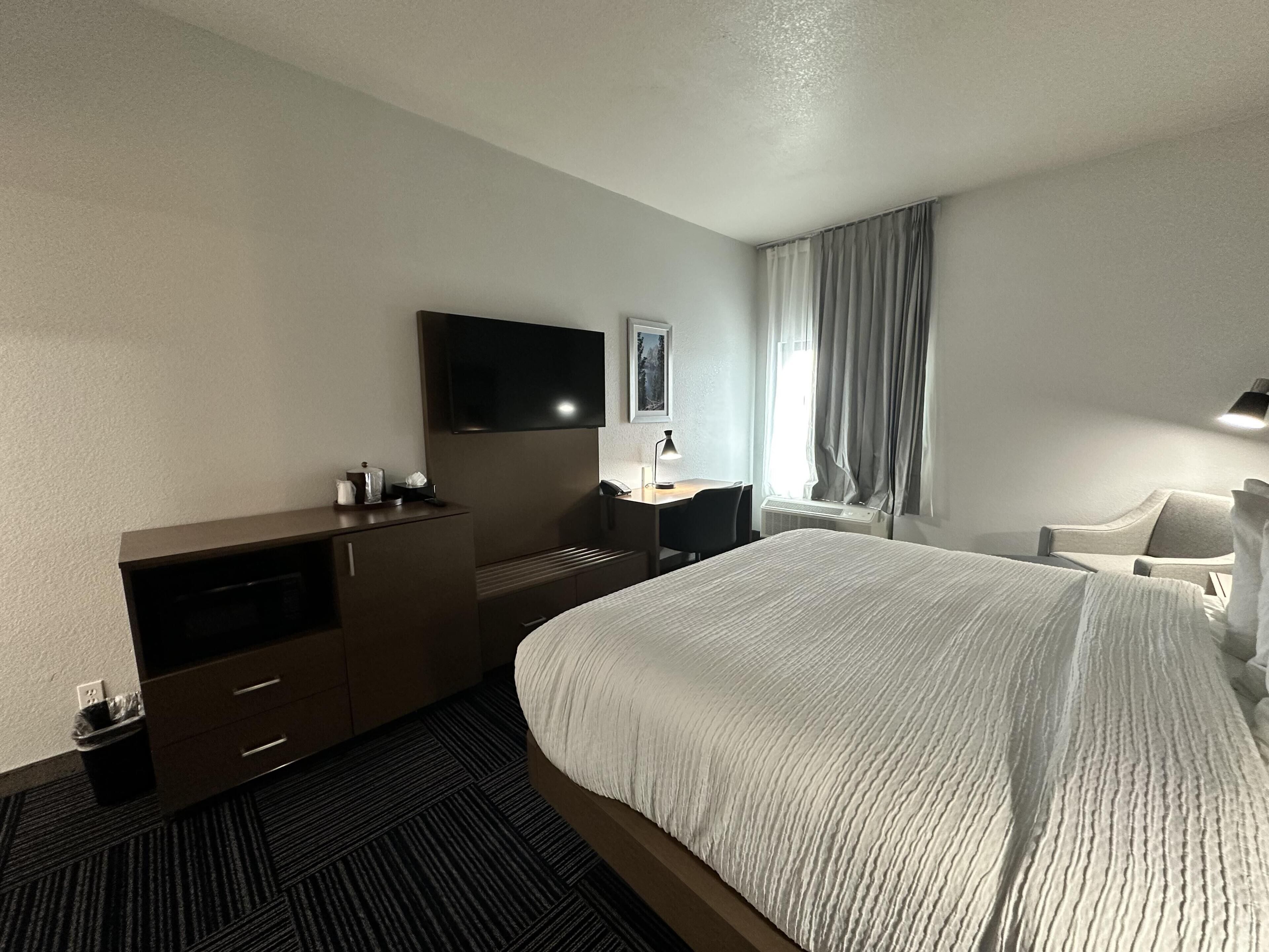 A hotel room with a bed, a desk, a TV, a chair, and a window with curtains.