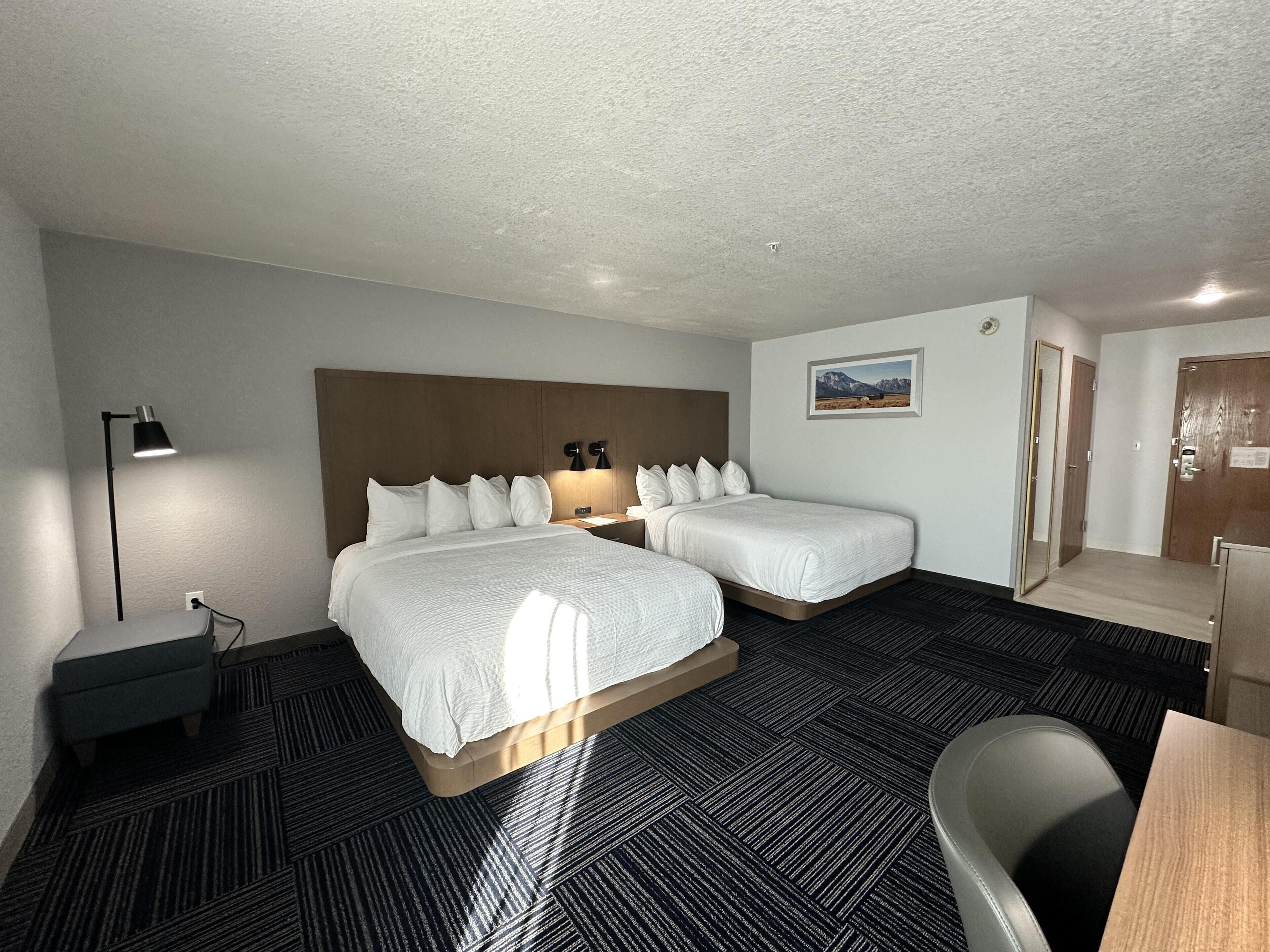 A hotel room with two beds, a desk, a chair, a lamp, and a picture on the wall.