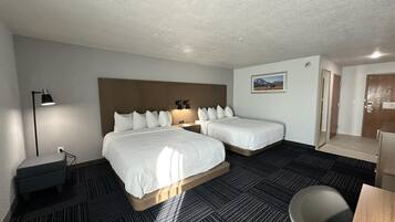 A hotel room with two beds, a desk, a chair, a lamp, and a picture on the wall.