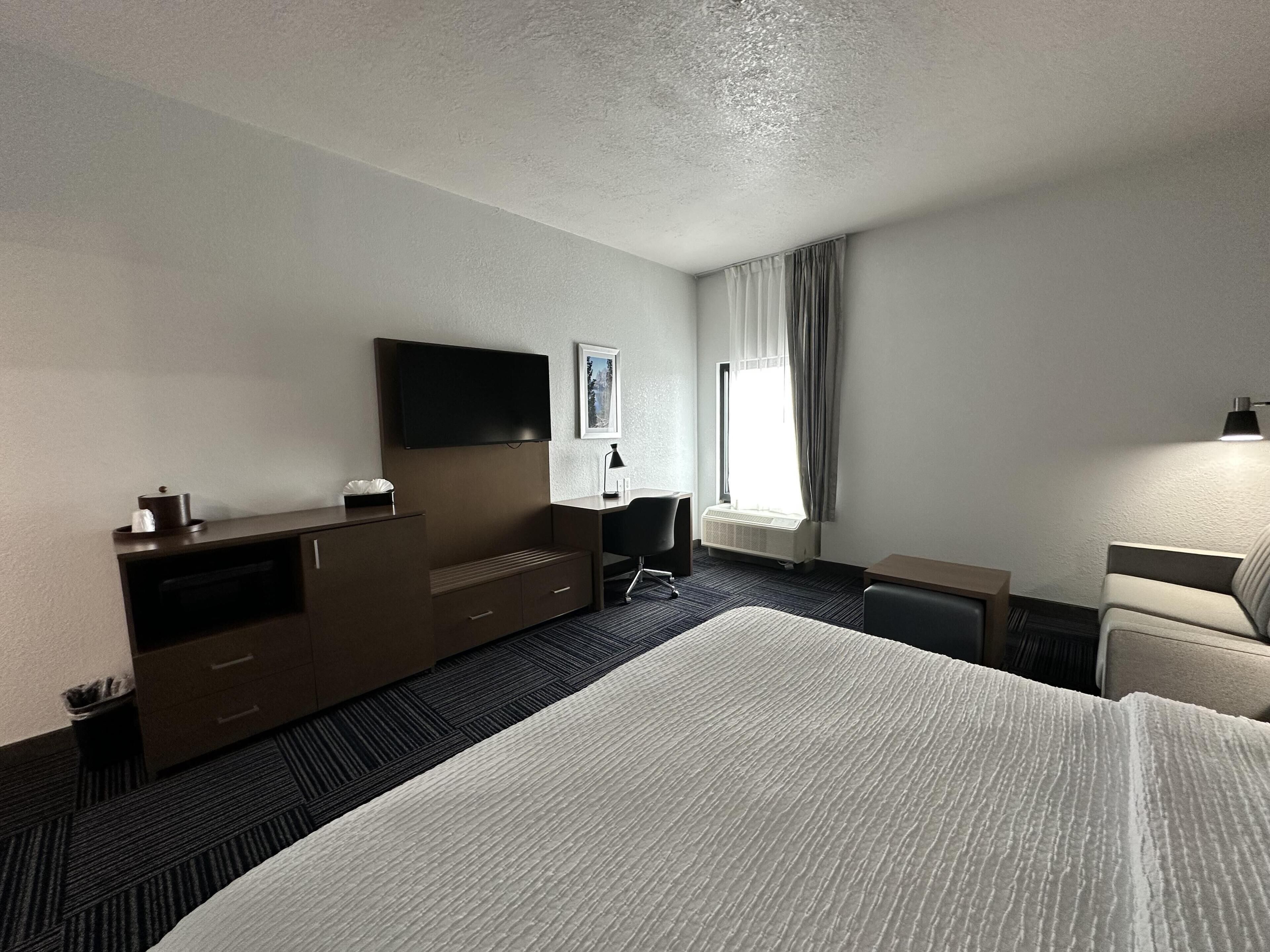Hotellihuone, jossa on sänky, työpöytä, tuoli, televisio ja ikkuna, jossa on verhot.