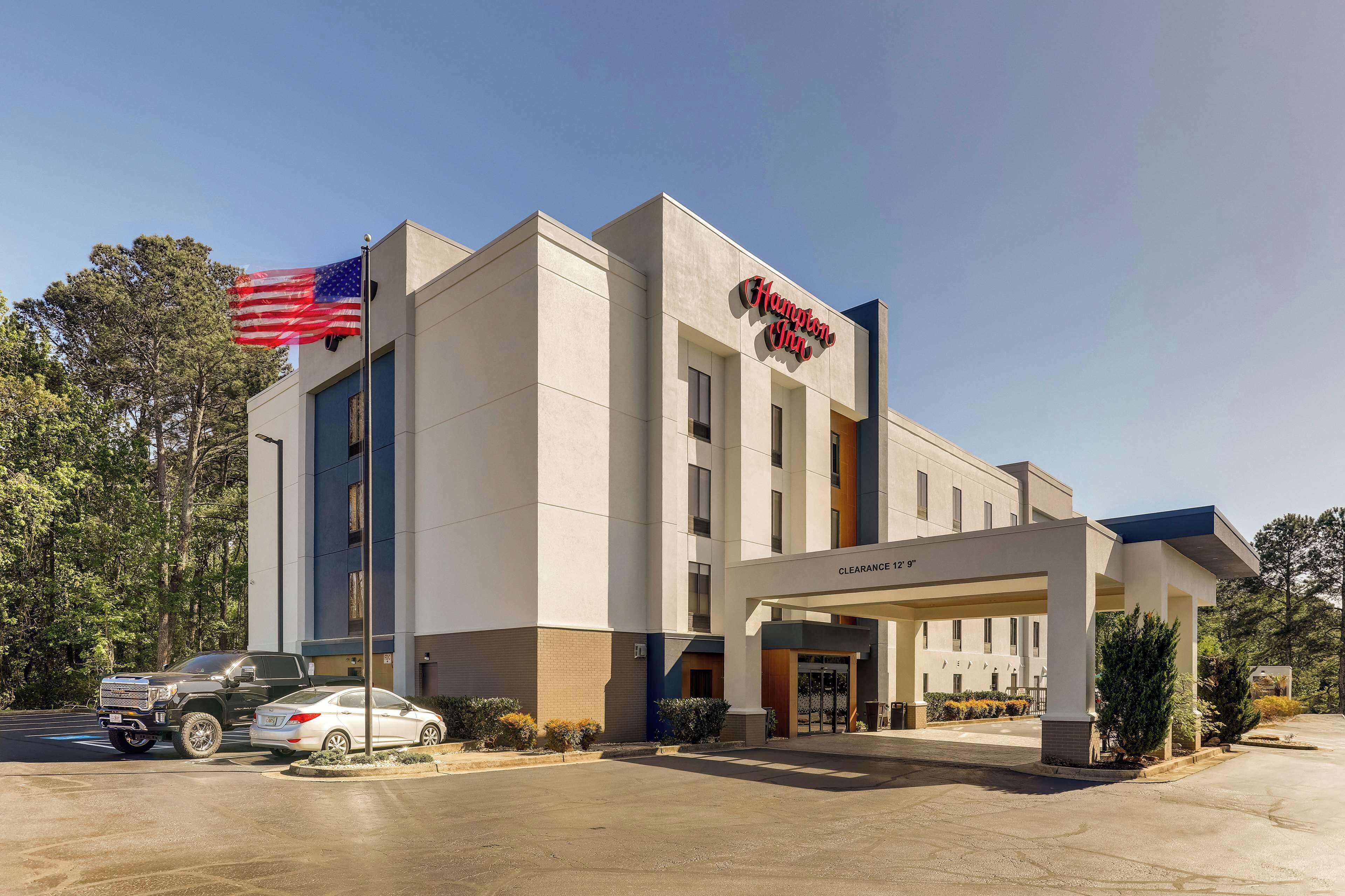 A Hampton Inn hotel with a clear entrance, a parking lot, and an American flag.
