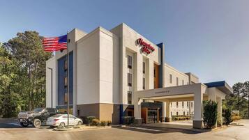 A Hampton Inn hotel with a clear entrance, a parking lot, and an American flag.