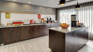 A modern kitchen with dark cabinets, a granite countertop, and a large island. There are various appliances and utensils on the counter, and a sign that reads "Let's Bake Some Memories."