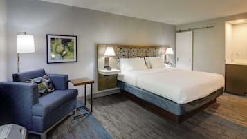 A hotel room with a bed, a desk, a chair, a lamp, and a painting on the wall.