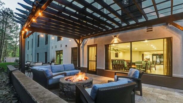 An outdoor patio with a fire pit, seating, and a covered area with string lights.
