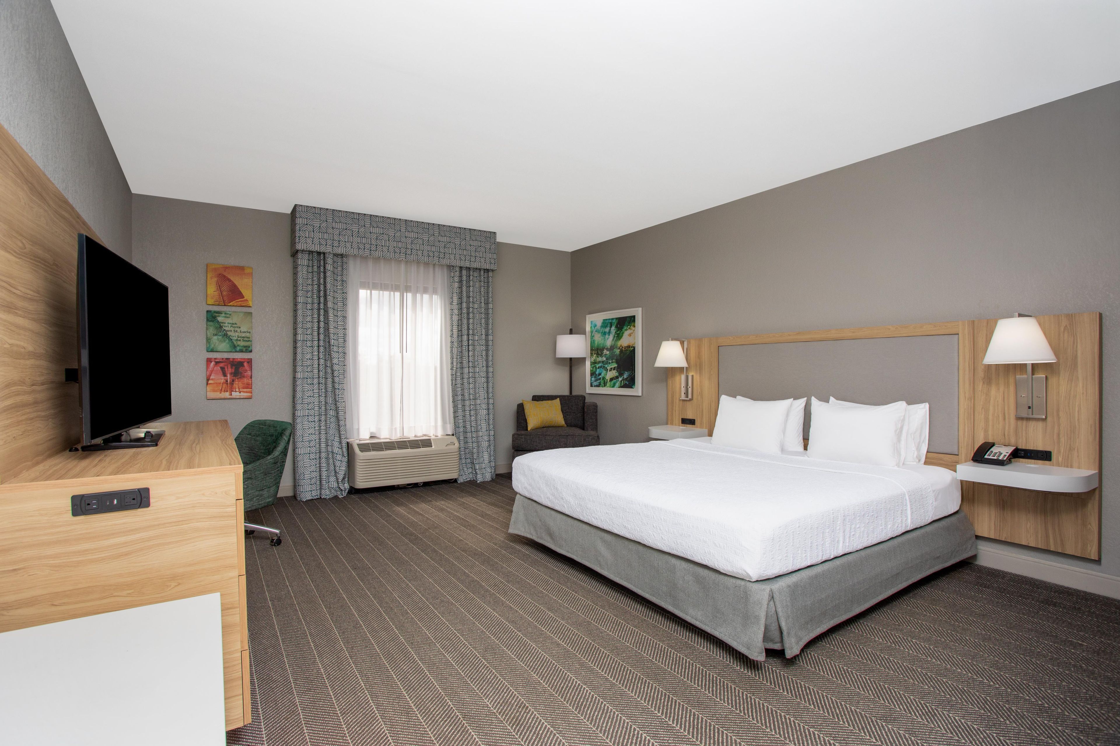Ein Hotelzimmer mit einem großen Bett, einem Flachbildfernseher, einem Schreibtisch und einem Sessel.