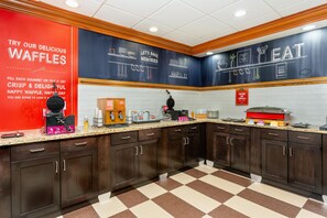 A kitchen area with waffle-making equipment, a red sign advertising waffles, and a caution sign for hot surfaces.