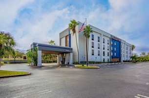 Un hotel moderno con techo plano, entrada cubierta y asta con la bandera estadounidense.