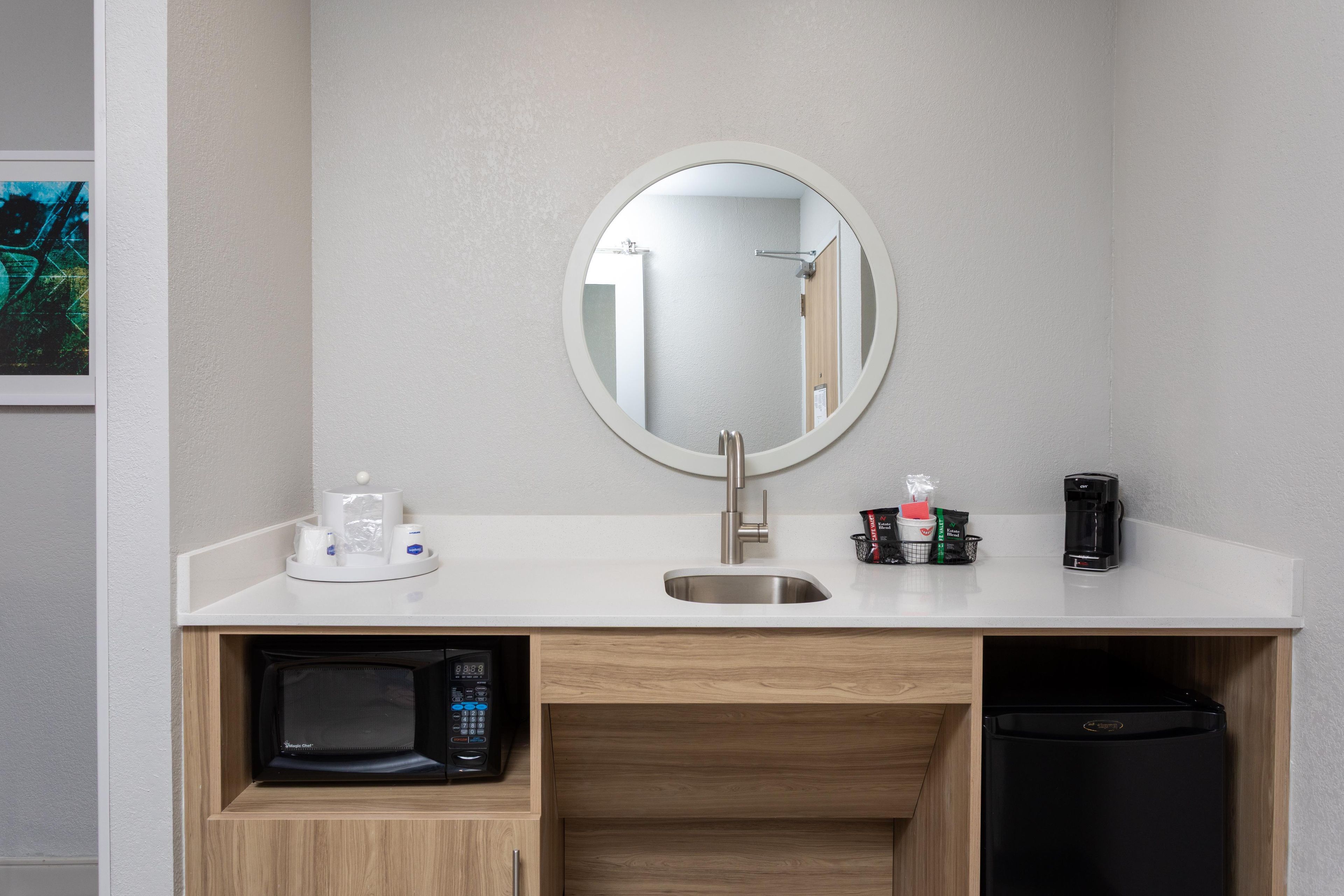 Een compacte kitchenette met een magnetron, koffiezetapparaat en een kleine koelkast.