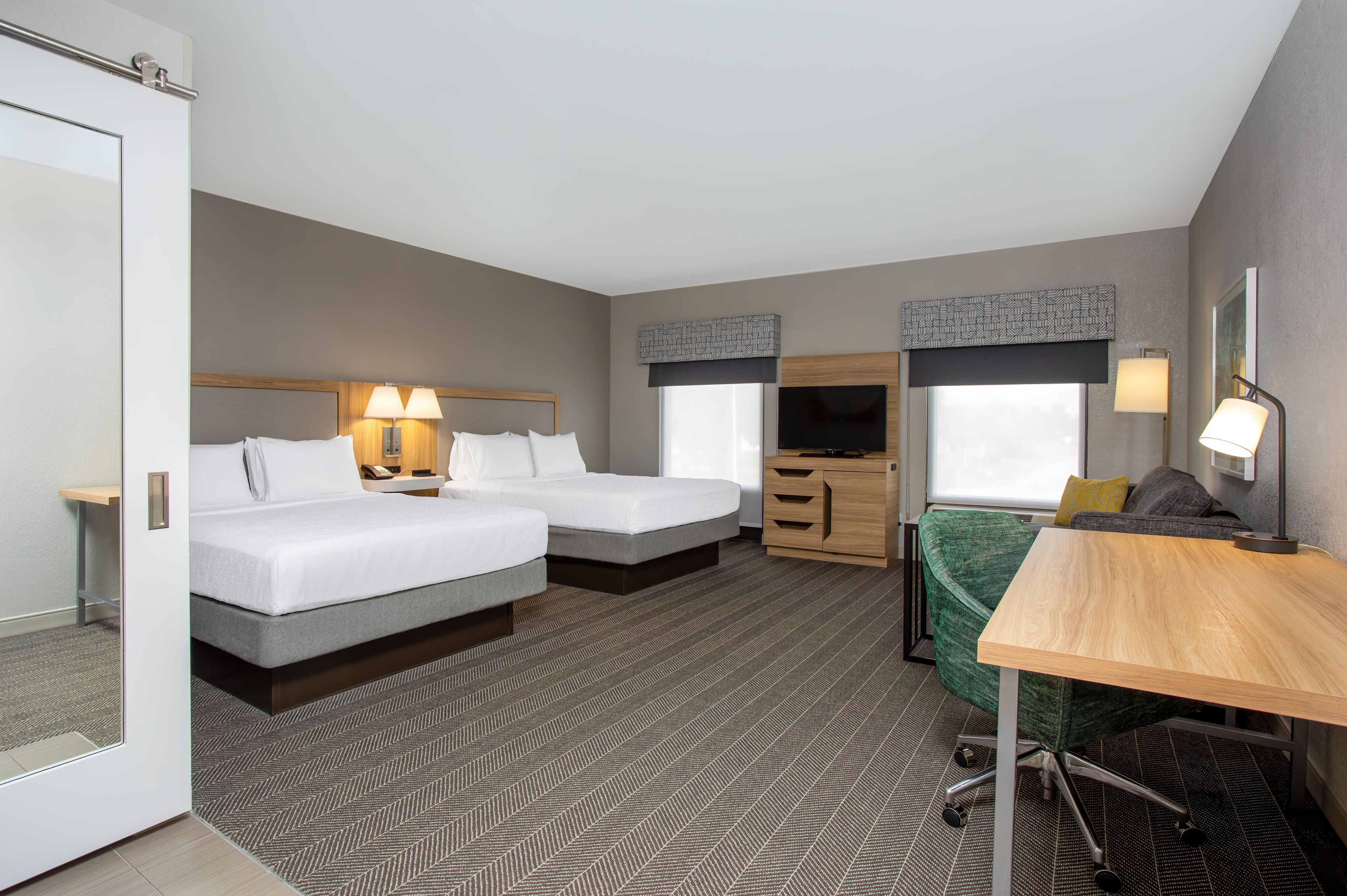 Een hotelkamer met twee bedden, een bureau, een stoel, een televisie en een raam met uitzicht.