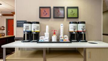 A coffee station with multiple coffee dispensers, a coffee machine, and a sign indicating breakfast hours.