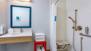 A bathroom with a sink, mirror, shower, and towel rack.