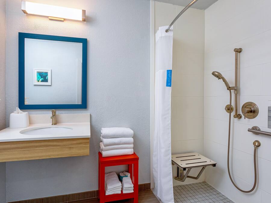 A bathroom with a sink, mirror, shower, and towel rack.