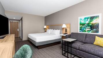 A hotel room with a bed, a sofa, a TV, a desk, and a painting on the wall.