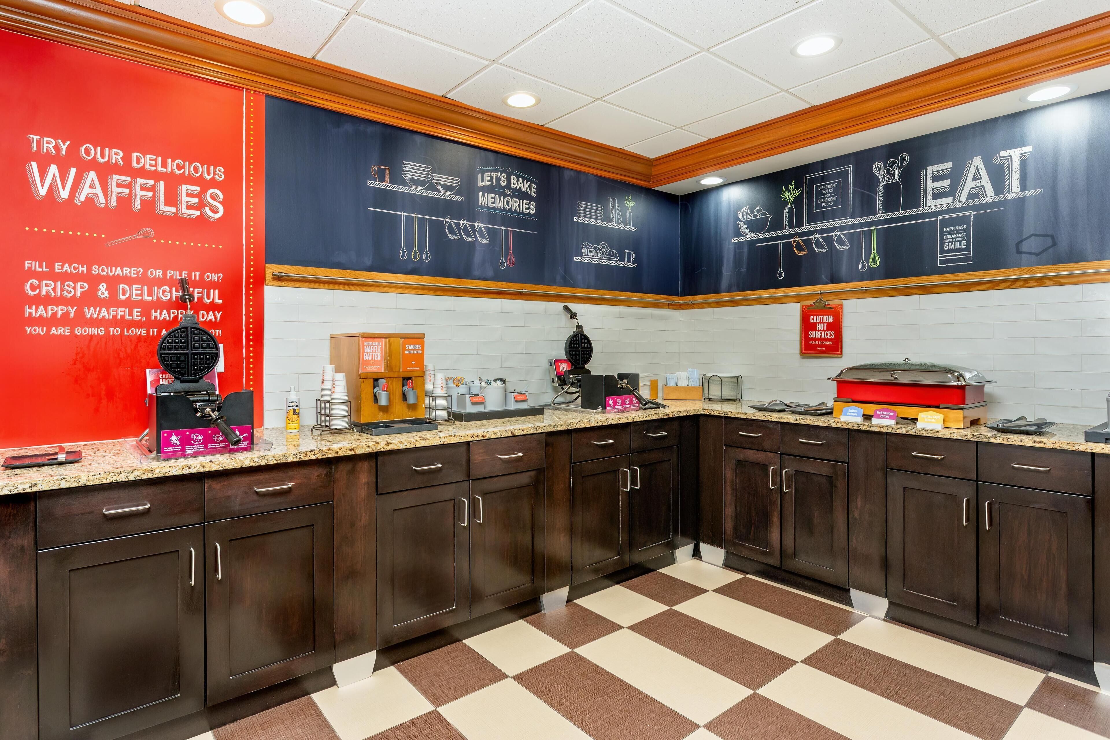 A kitchen with dark wooden cabinets, a checkered floor, and a waffle-making station.