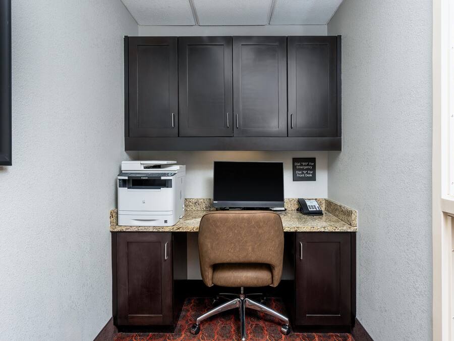 A corner office with a dark wood desk, a printer, a computer monitor, and a phone.