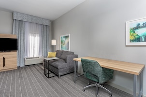 Habitación de hotel con sofá, escritorio, televisión, lámpara y un cuadro en la pared.