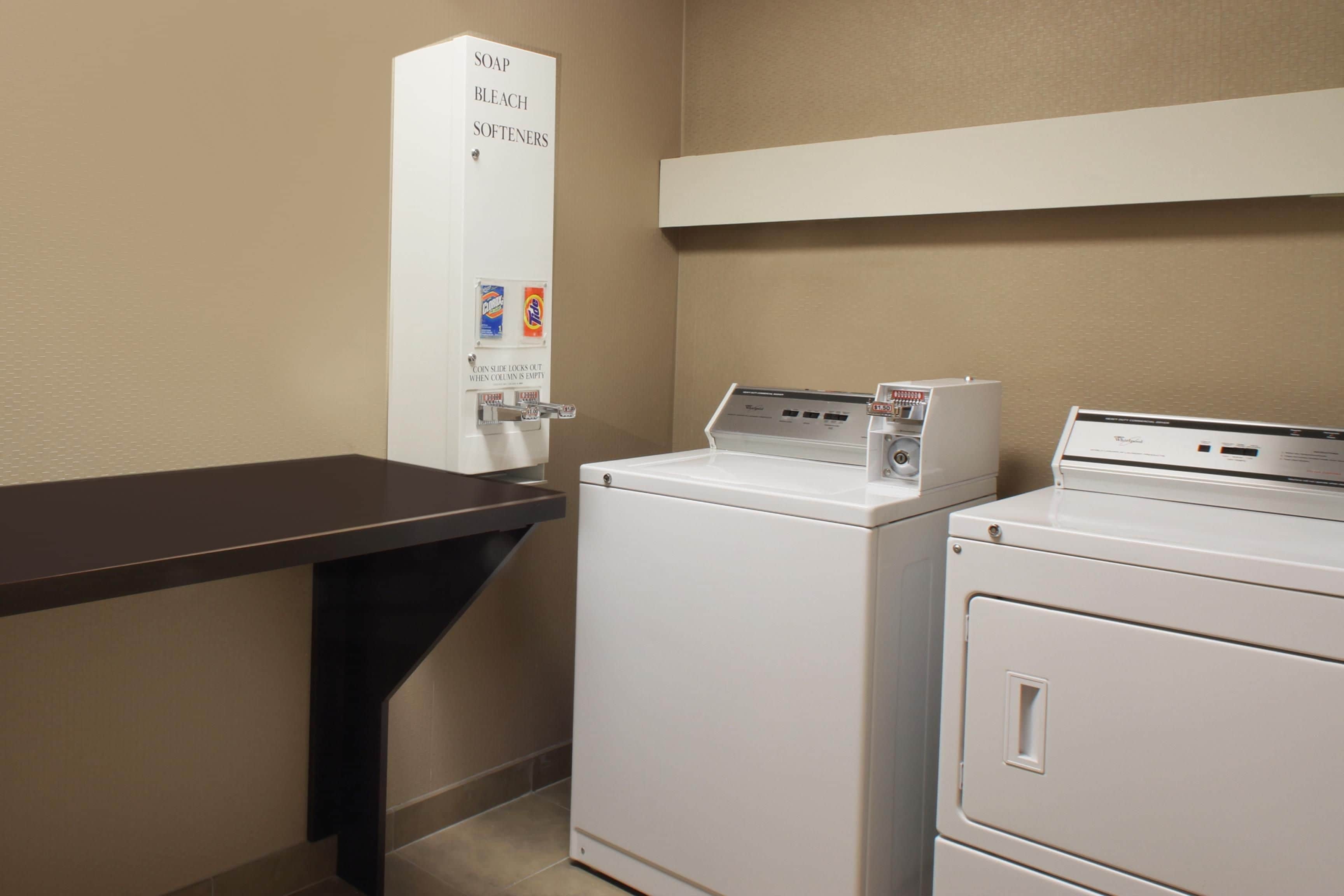 A laundry area with a washing machine, dryer, and a soap and bleach dispenser.