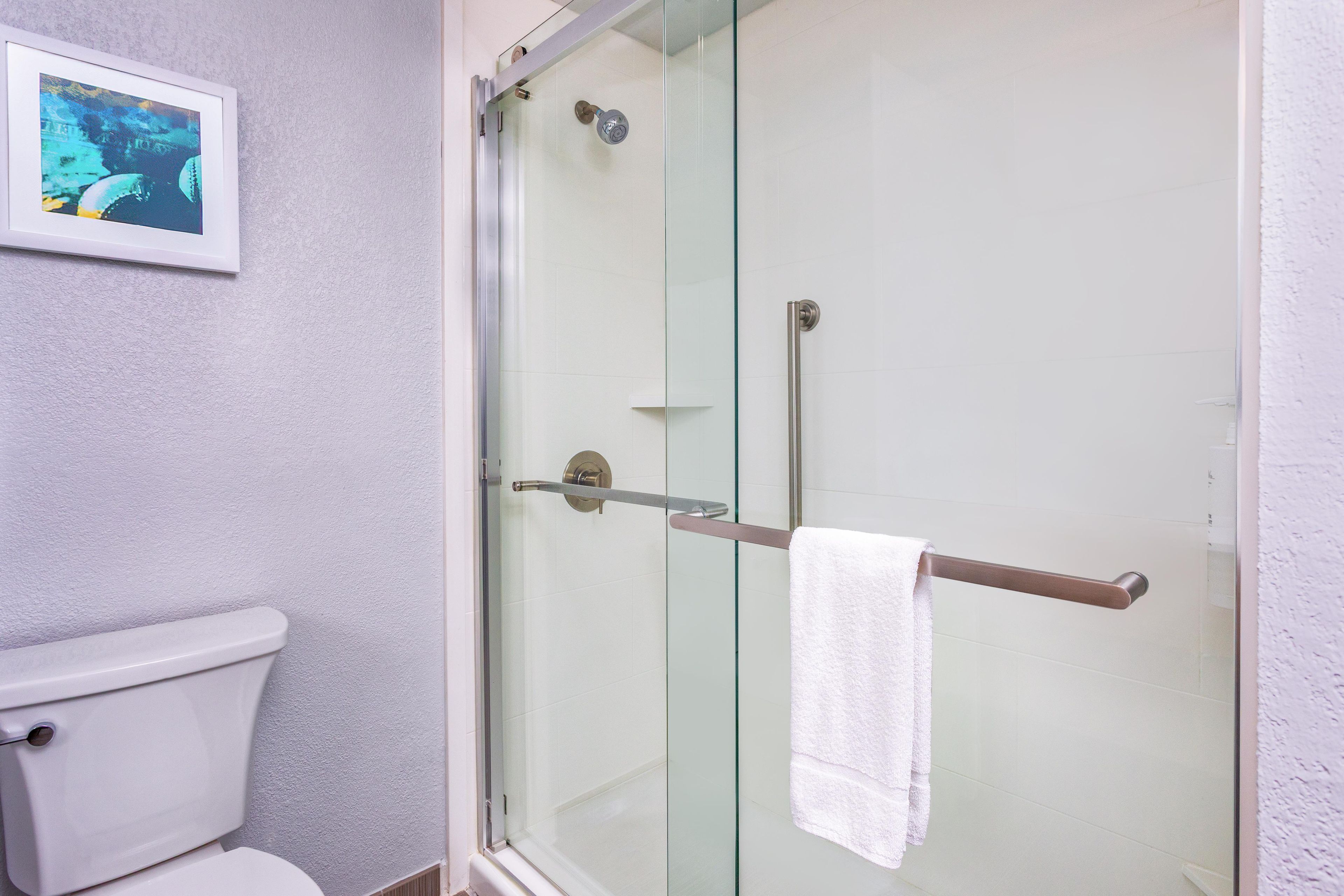 A bathroom with a glass-enclosed shower, a white toilet, and a towel rack with a white towel.