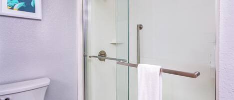 A bathroom with a glass-enclosed shower, a white toilet, and a towel rack with a white towel.