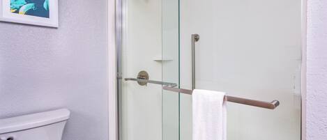 A bathroom with a glass shower enclosure, a white toilet, and a framed picture on the wall.