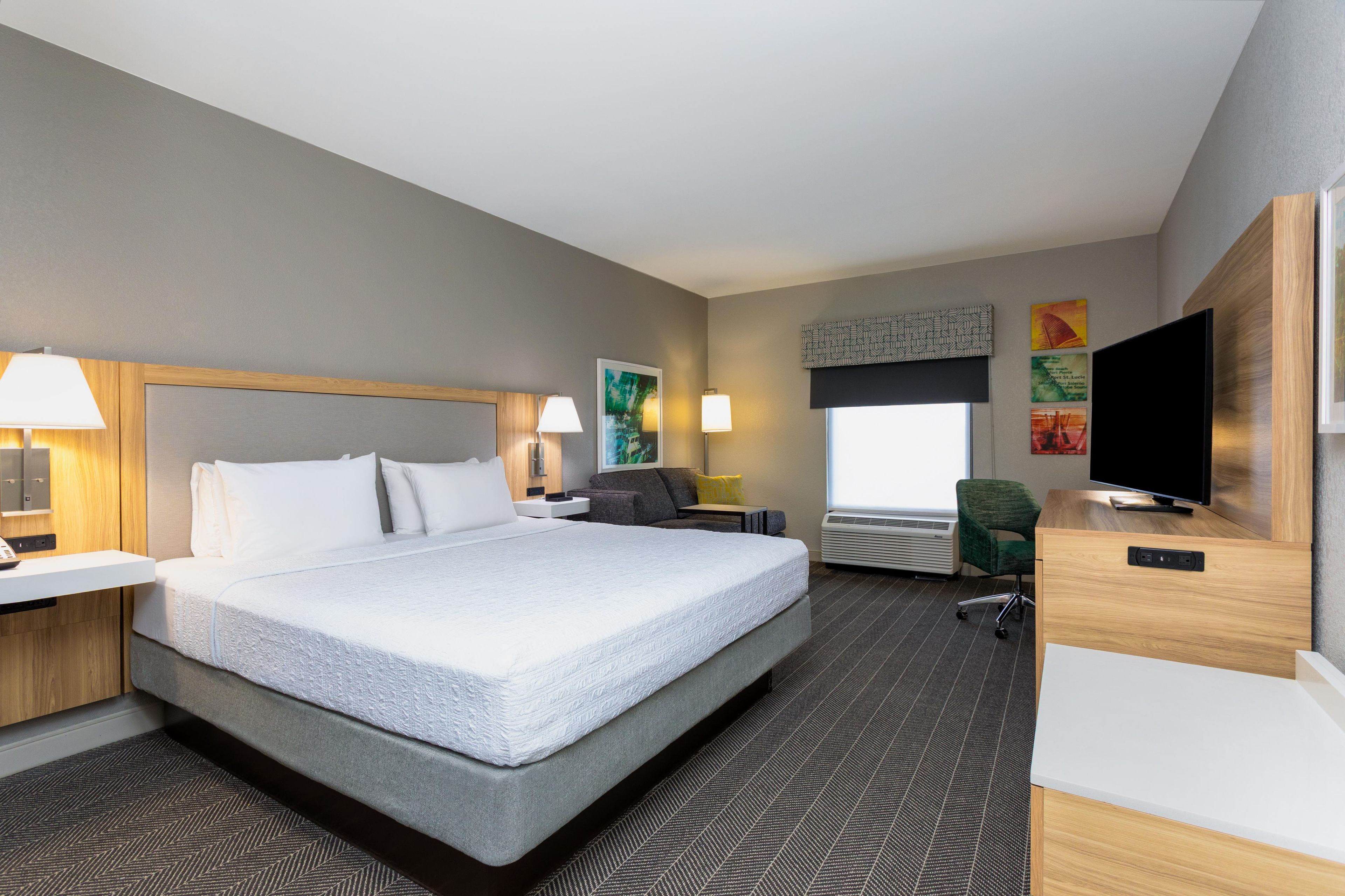 Ein Hotelzimmer mit einem großen Bett, einem Schreibtisch, einem Sessel, einem Fernseher und Bildern an den Wänden.