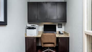 A corner office with a dark wood desk, a brown leather chair, a printer, a monitor, and a phone.