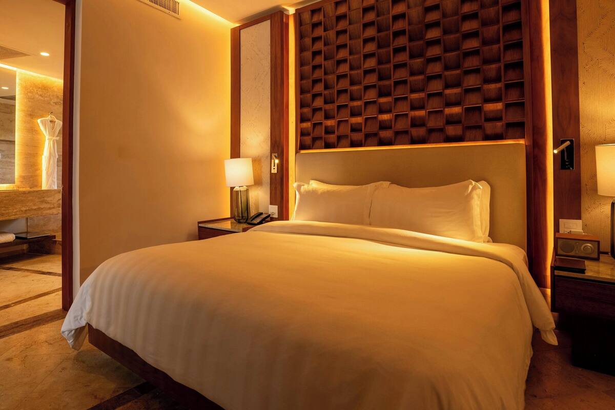 Una habitación de hotel con una cama grande, cabecera de madera, mesitas de noche con lámparas y un espejo.