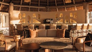 Un espace salon accueillant, doté d’un toit de chaume, de sièges confortables et d’un mur décoré de luminaires en forme de bouteille.