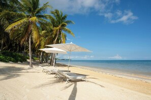 Di pantai, pasir putih, kursi berjemur, dan payung pantai