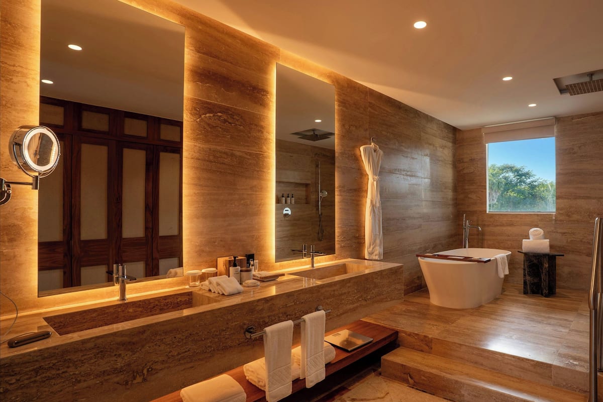 Un baño moderno con un espejo grande, lavamanos dobles, una bañera independiente y un mueble de tocador con espejo.