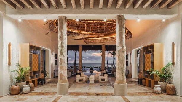 Un vestíbulo amplio con vista al mar, que incluye una zona de estar, columnas grandes y un techo con diseño tejido.