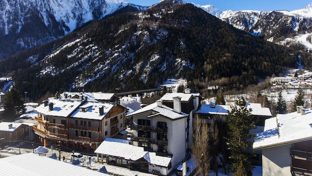 A snow-covered mountain with a ski resort in the foreground, featuring multi-story buildings with balconies and ski lifts visible.