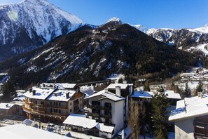 A snow-covered mountain with a ski resort in the foreground, featuring multi-story buildings with balconies and ski lifts visible. - Hotel Les Jumeaux Courmayeur (Courmayeur)