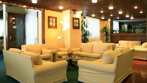 A spacious living area with multiple sofas and a coffee table, featuring a wooden ceiling and wall-mounted lamps.