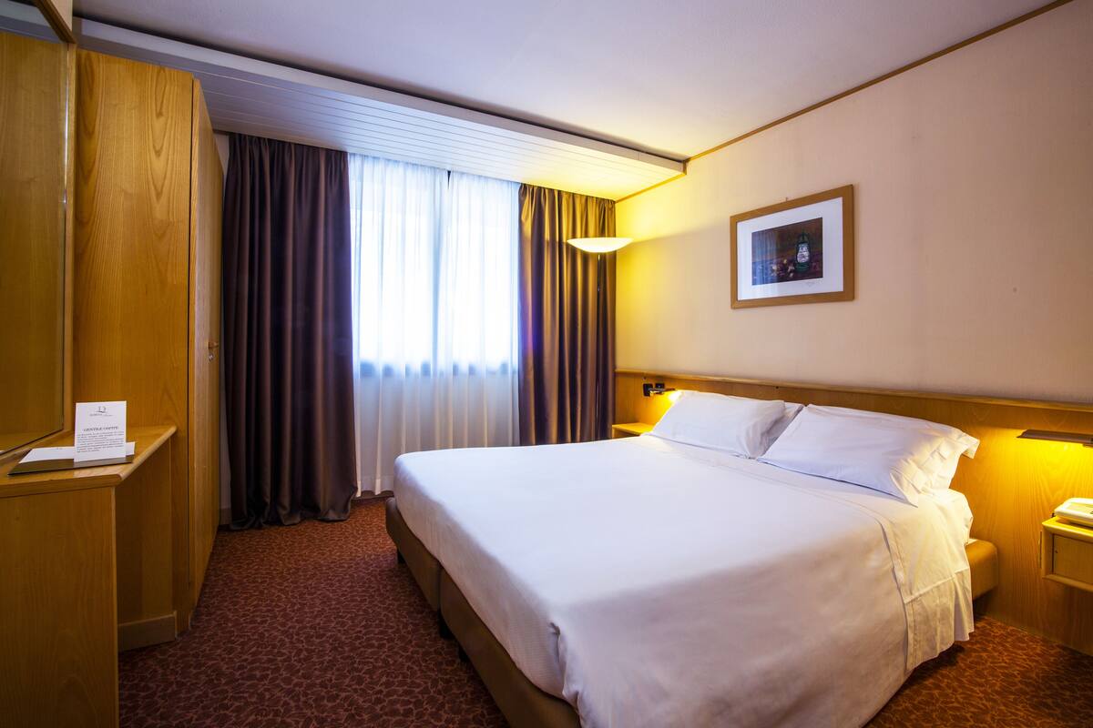 Une chambre d’hôtel avec un grand lit, un bureau, une chaise, une table de chevet, une lampe et un tableau encadré au mur.