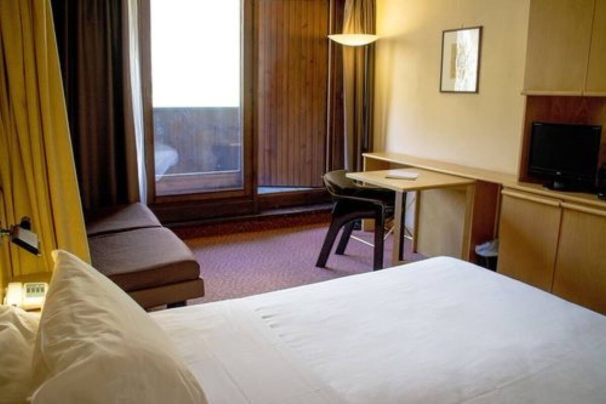 Une chambre d’hôtel équipée d’un lit, d’un bureau, d’une chaise, d’une télévision et d’une fenêtre avec des rideaux.